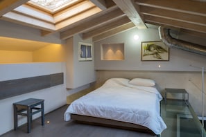 Ein Schlafzimmer mit Dachfenster, einem Bett, einem Nachttisch und einem Bild an der Wand.