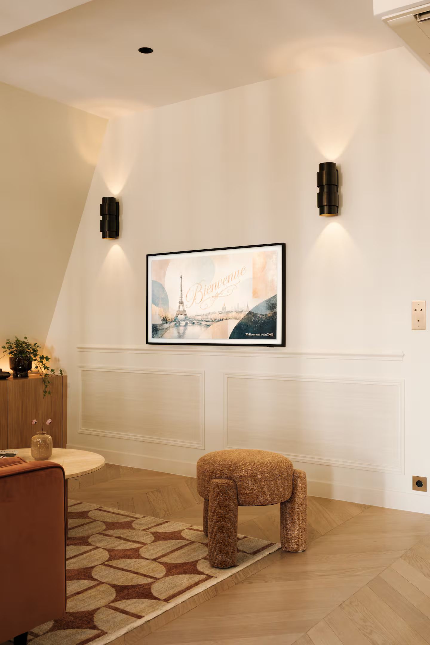 A room with a framed picture of the Eiffel Tower, a bench, and two wall-mounted lights.