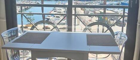A balcony with a table and chairs, overlooking a marina with boats and palm trees.
