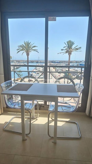 Ein Balkon mit Tisch und Stühlen, mit Blick auf einen Hafen voller Boote und Palmen.