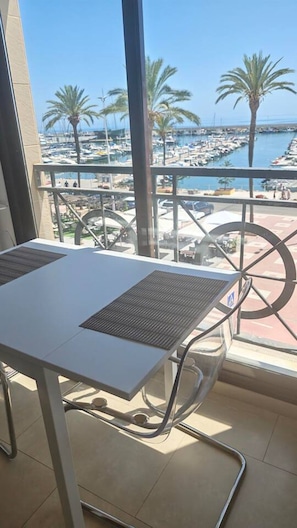 Ein Balkon mit Tisch und Stühlen, mit Blick auf einen Yachthafen mit Booten und Palmen.