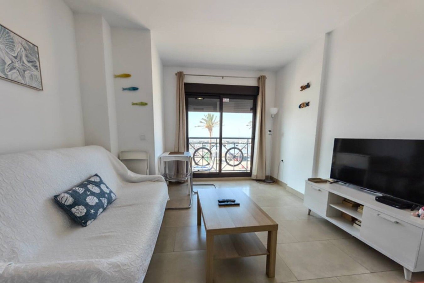 Ein Wohnzimmer mit Sofa, Couchtisch, Fernseher und einem Balkon mit Blick.