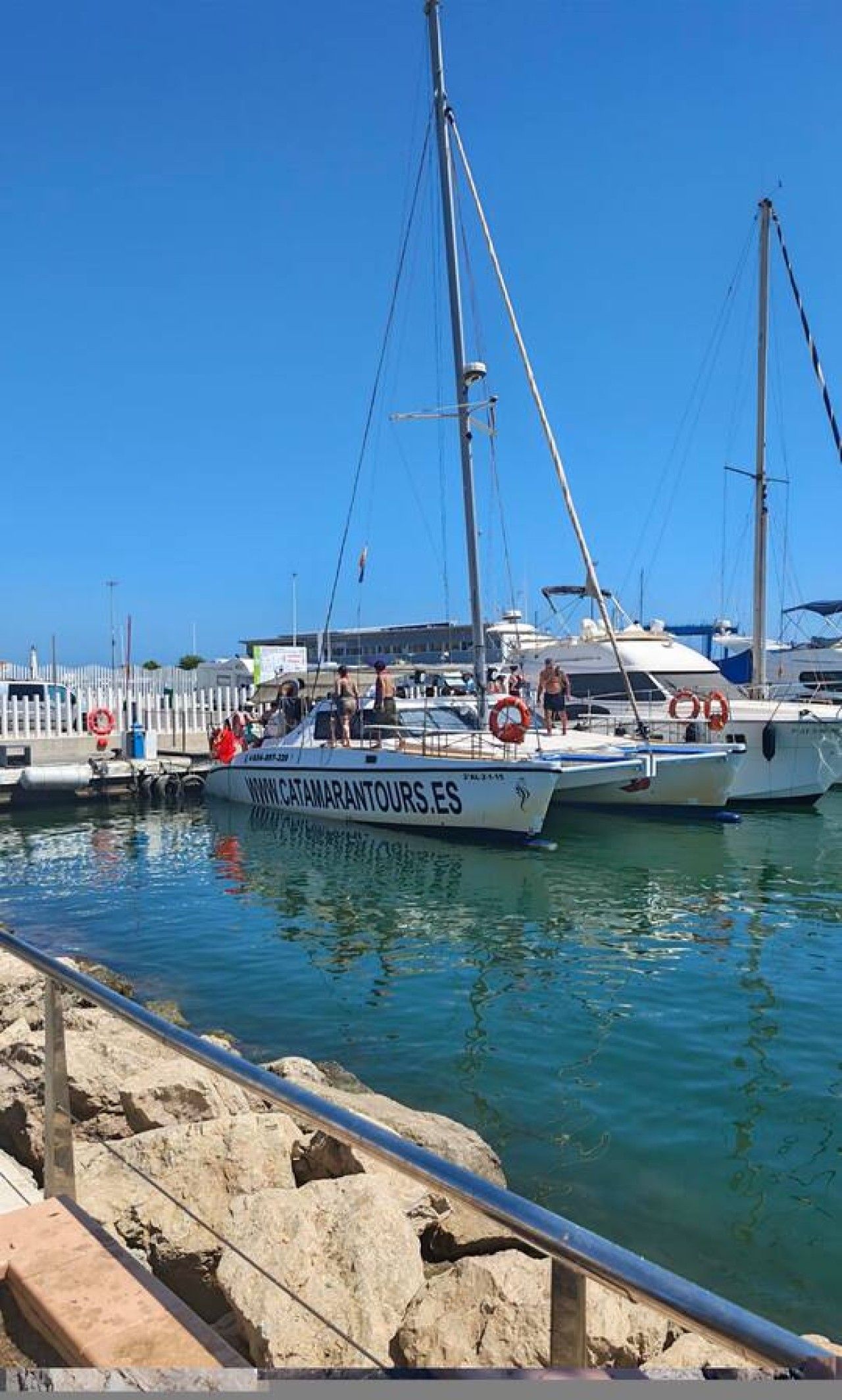 Un port de plaisance avec des bateaux amarrés, un ciel dégagé et une côte rocheuse.