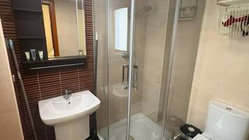 A modern bathroom with a glass-enclosed shower, a white sink, and a toilet.
