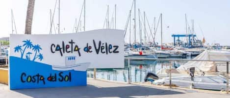 A sign for 'Calle de Velez' with a marina in the background.
