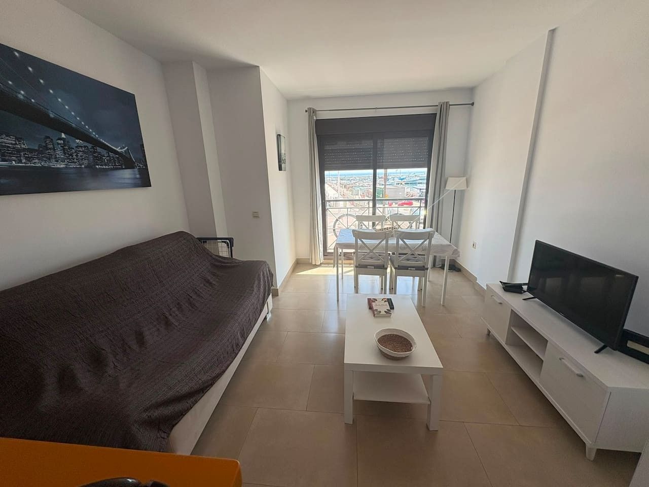 Een moderne woonkamer met een bank, een salontafel, een televisie en een balkon met uitzicht op de stad.