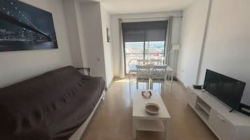 Een moderne woonkamer met een bank, een salontafel, een televisie en een balkon met uitzicht op de stad.