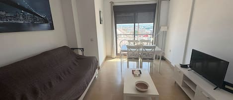 A modern living room with a sofa, a coffee table, a TV, and a balcony with a city view.