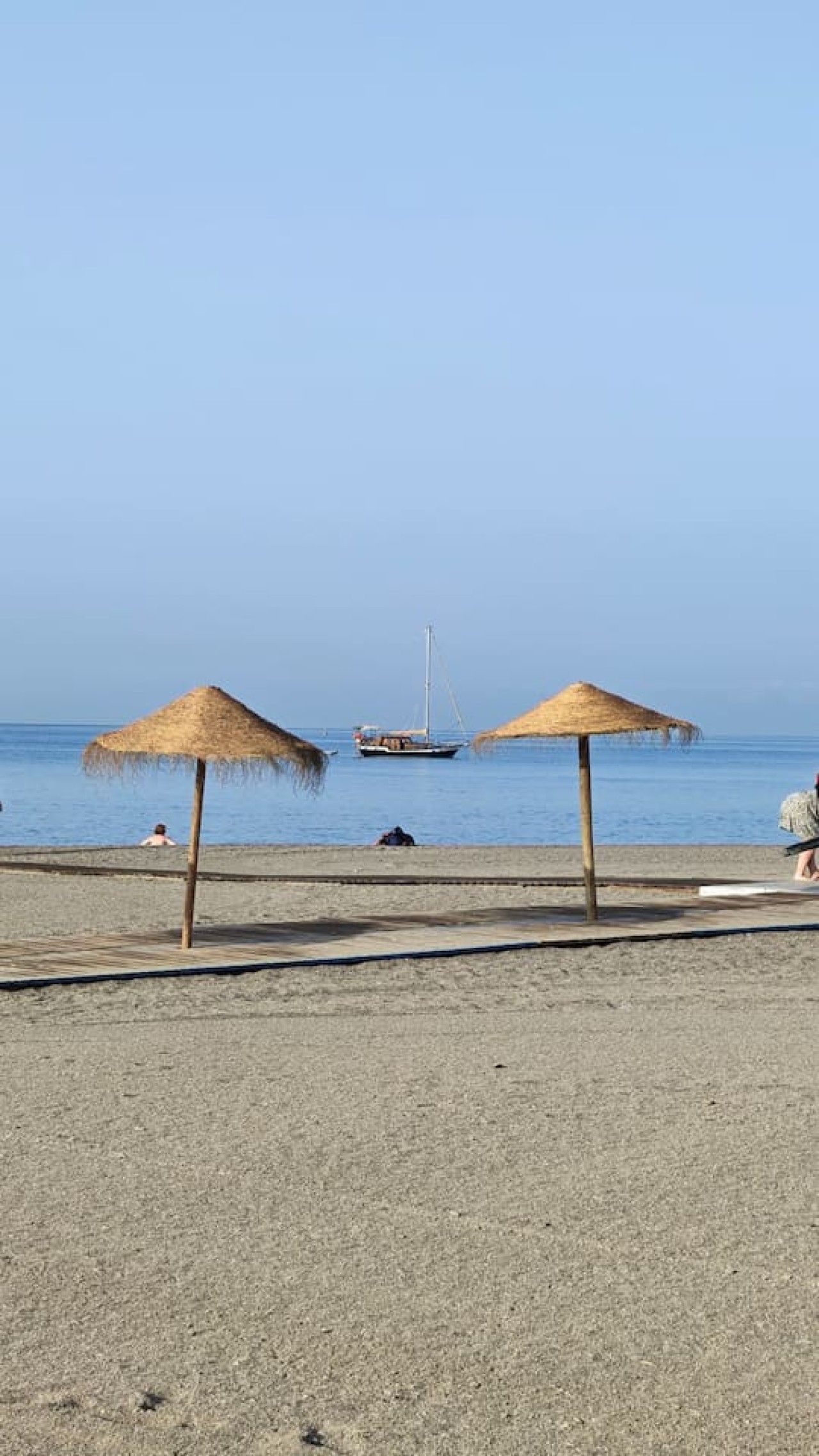 Ein Strand mit zwei Reetsonnenstühlen und einem Segelboot in der Ferne.