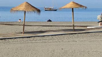 Ein Strand mit zwei Reetsonnenstühlen und einem Segelboot in der Ferne.