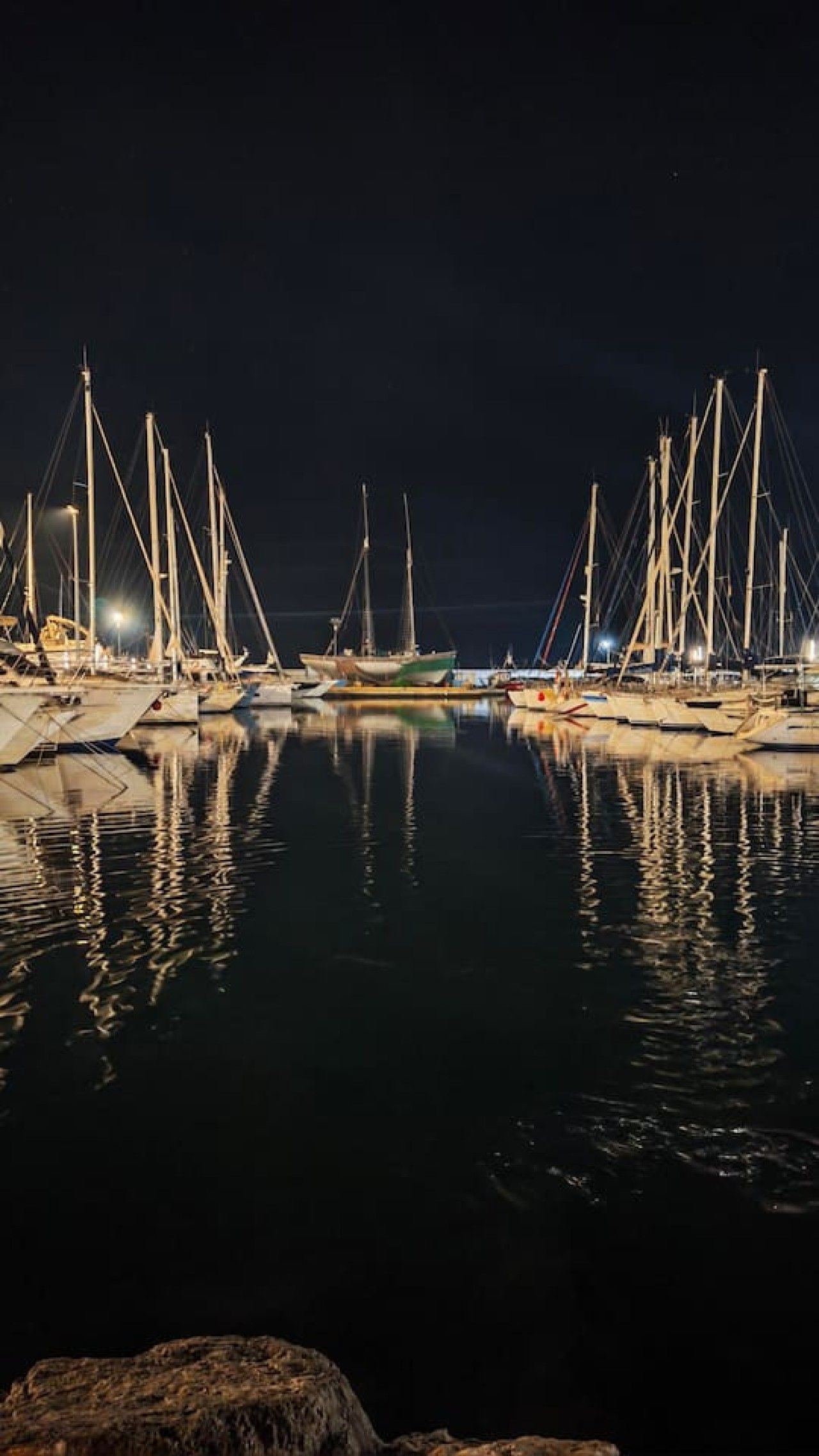 Ein Yachthafen bei Nacht mit vertäuten Booten und ruhigem Wasser, das die Lichter reflektiert.