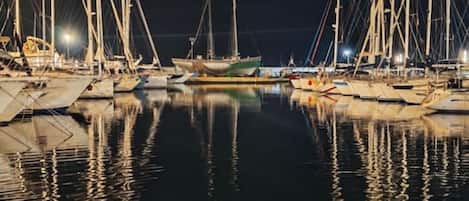 Una marina de noche con barcos amarrados y agua tranquila que refleja las luces.