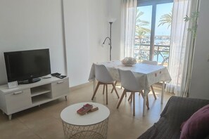 A modern living room with a flat-screen TV, a dining table with chairs, a small round table with books, and a view of the sea through large windows. - Mar Y Sol Caleta Brisa 2B (Algarrobo-Costa)