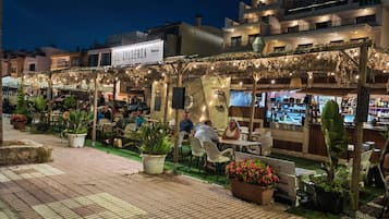 Un espacio al aire libre con mesas, sillas, bar y plantas en macetas.