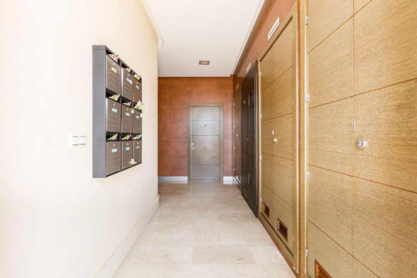 Un pasillo con una fila de casilleros a la izquierda y una puerta de madera a la derecha.