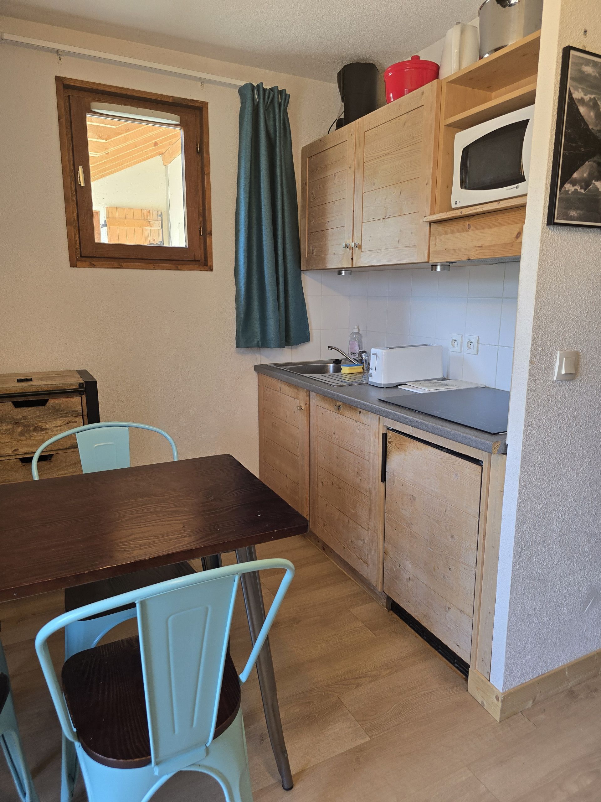 Una cocina compacta con armarios de madera, un microondas y un comedor con una mesa y sillas.