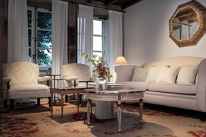 A room with a round coffee table, two armchairs, a sofa, a mirror, and a window with curtains. - Pazo Recimil (Lugo)