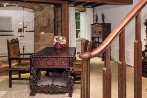 A dining area with a wooden table and chairs, a vase of flowers, and a staircase leading to another room. - Pazo Recimil (Lugo)