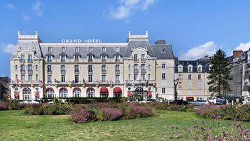 Un grand bâtiment historique, surmonté d’une enseigne indiquant « GRAND HÔTEL », qui présente une architecture classique avec de nombreuses fenêtres et des balcons.
