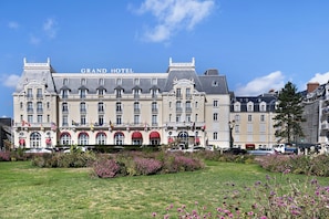 Un grand bâtiment historique, surmonté d’une enseigne indiquant « GRAND HÔTEL », qui présente une architecture classique avec de nombreuses fenêtres et des balcons.