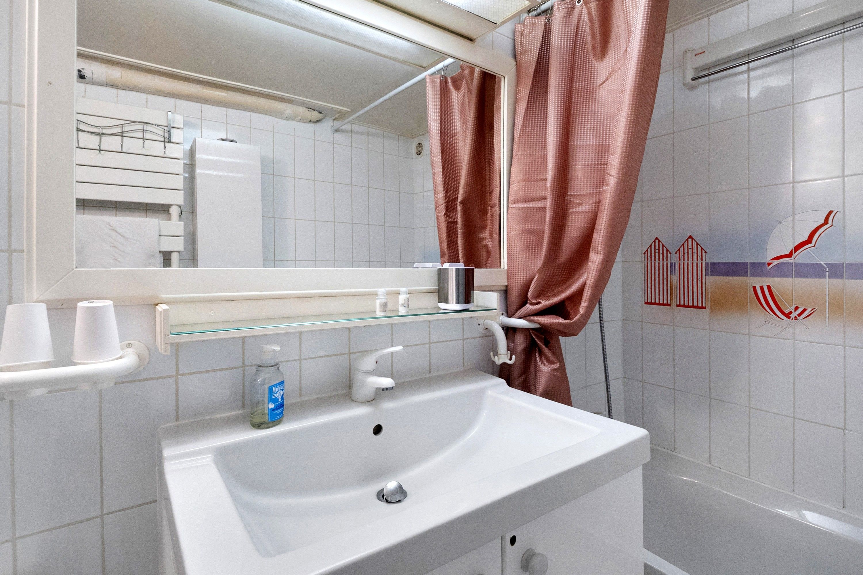 Een badkamer met een wit wastafel, een spiegel, een glazen plank en een douchegordijn.