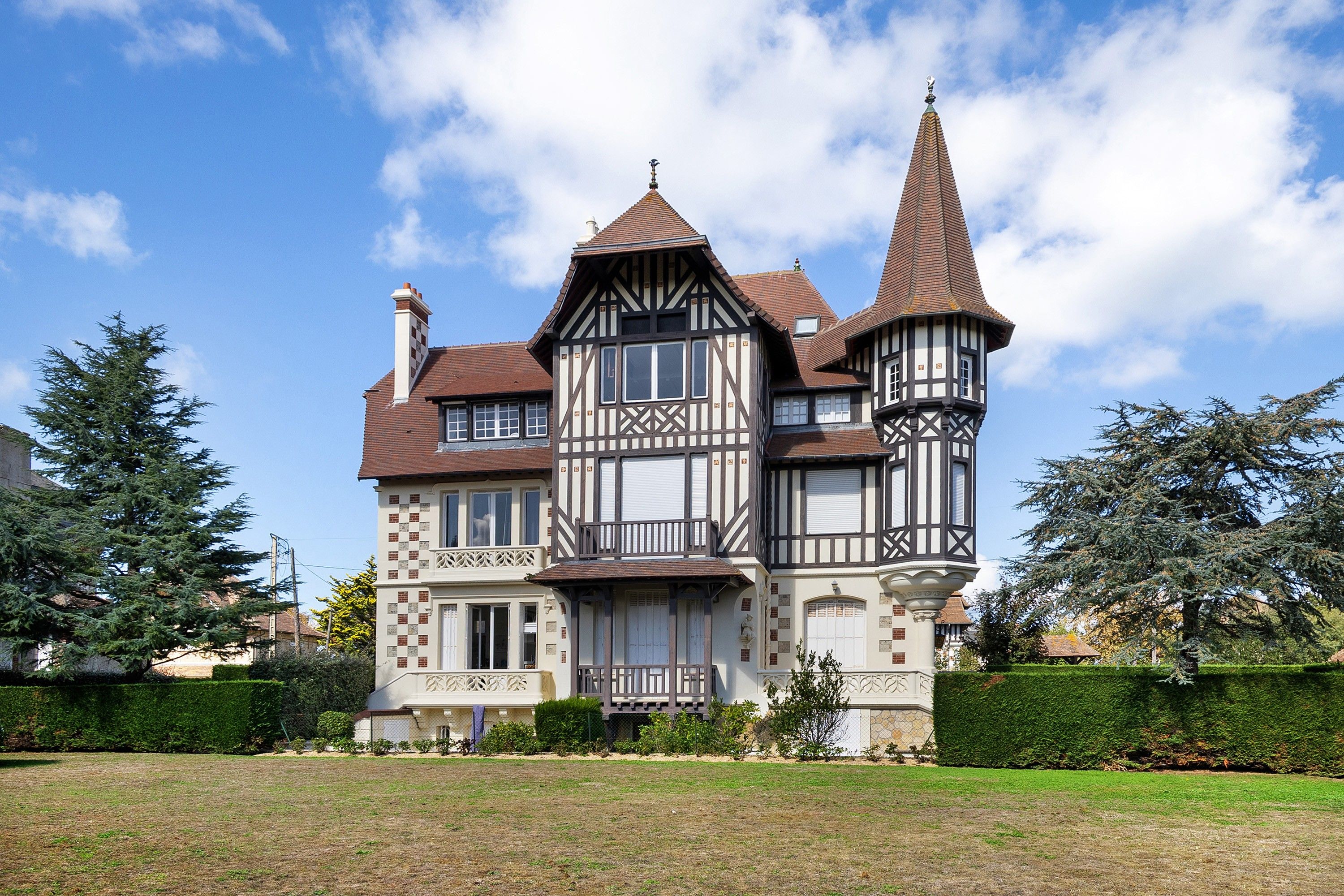 Ein großes, historisches Haus mit mehreren Stockwerken, einem markanten Turm und einem gepflegten Rasen.