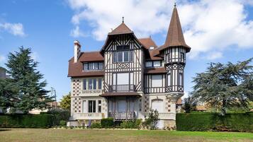 Ein großes, historisches Haus mit mehreren Stockwerken, einem markanten Turm und einem gepflegten Rasen.