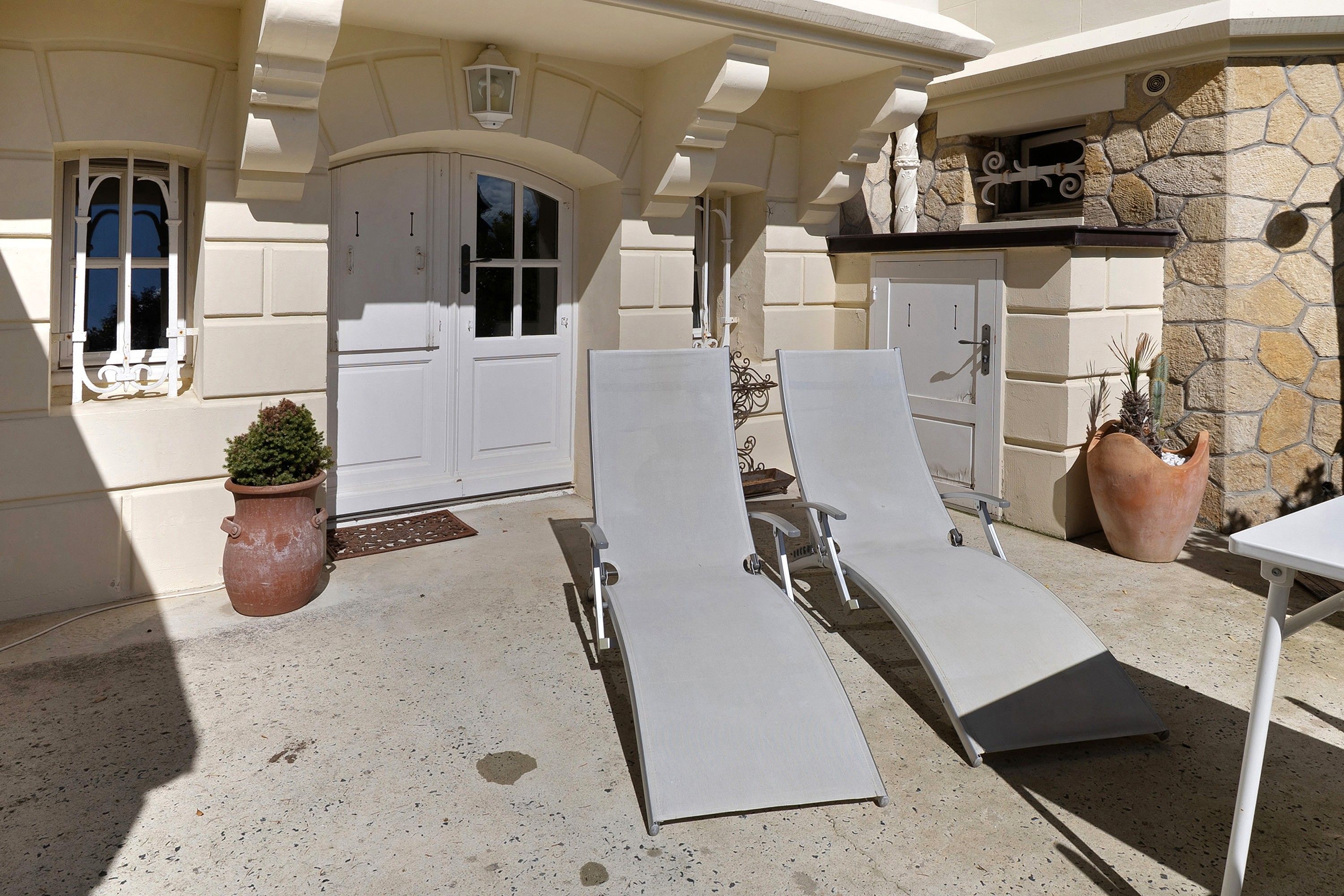 Une terrasse avec deux chaises longues, une plante en pot et un mur en pierre.