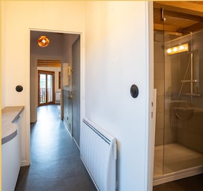 Ein Flur, der zu einem Badezimmer mit Dusche, Heizkörper und einer Tür zu einem weiteren Raum führt.