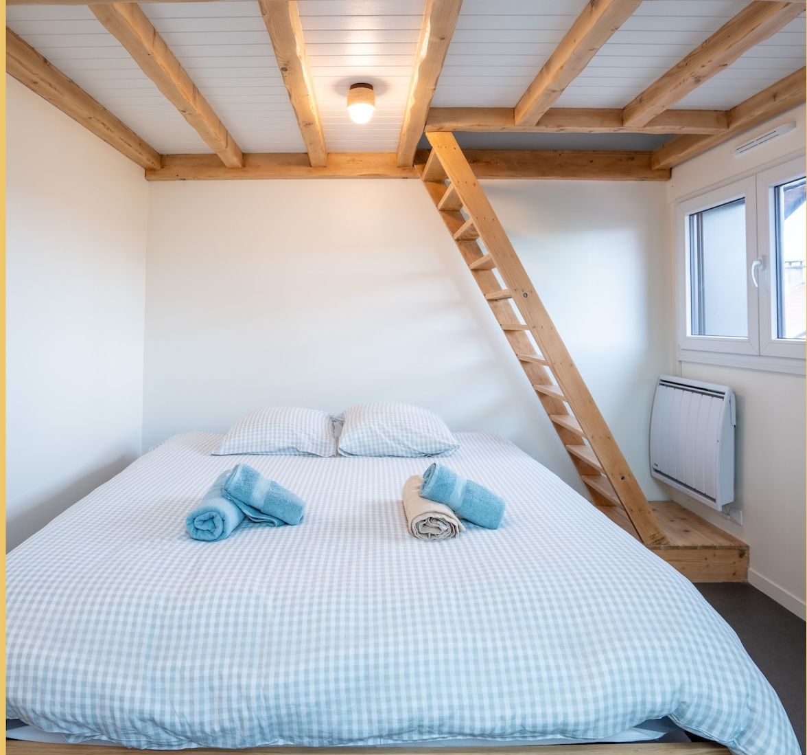 A bedroom with a bed, a wooden ladder, and a window.