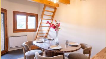 A dining area with a round table, chairs, a vase with flowers, a ladder, and a window.