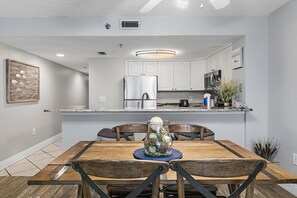 A dining area with a wooden table and chairs, a ceiling fan, and a kitchen in the background. - Sundestin 1803 (Destin)