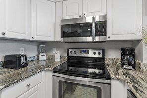 A modern kitchen with white cabinetry, a built-in microwave, a toaster, a blender, a coffee maker, and a stove. - Sundestin 1803 (Destin)