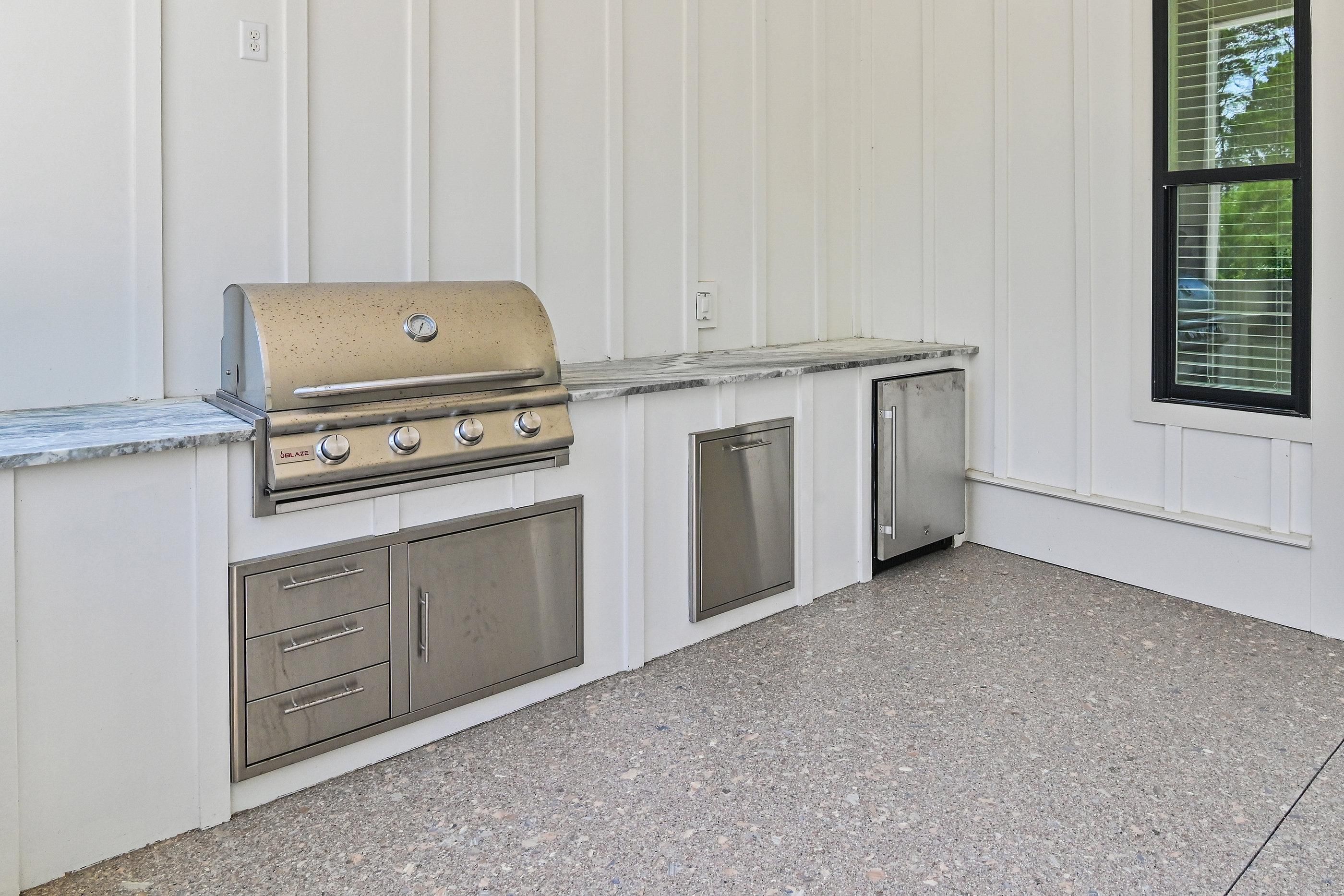 A kitchen with a built-in grill, stainless steel cabinets, and a window with blinds.