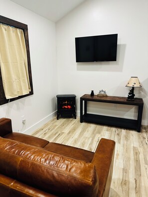 Un salon avec un canapé en cuir marron, un meuble de rangement noir pour appareils électroniques, une cheminée et un téléviseur fixé au mur.