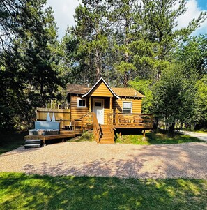 Une cabane en rondins avec une terrasse, un petit porche et une allée gravillonnée.