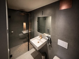 Un baño moderno con ducha envuelta en vidrio, un lavabo blanco y un espejo grande.