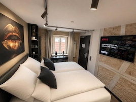 Una habitación de hotel con dos camas, un televisor montado en la pared y una ventana con cortinas.