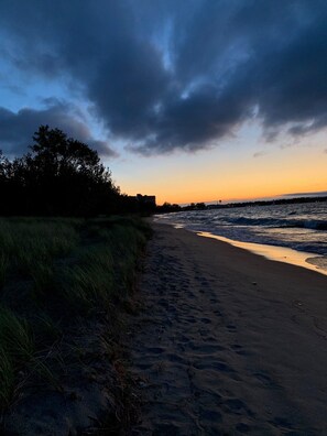 A beach with a path leading to the water, trees on the left, and a building in the distance.