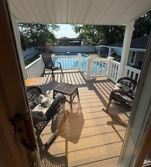 A covered deck with a pool, outdoor furniture, and a view of a residential area.