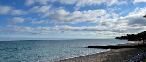 Una playa con costa rocosa, un muelle de madera y un cartel que indica acceso a la playa.