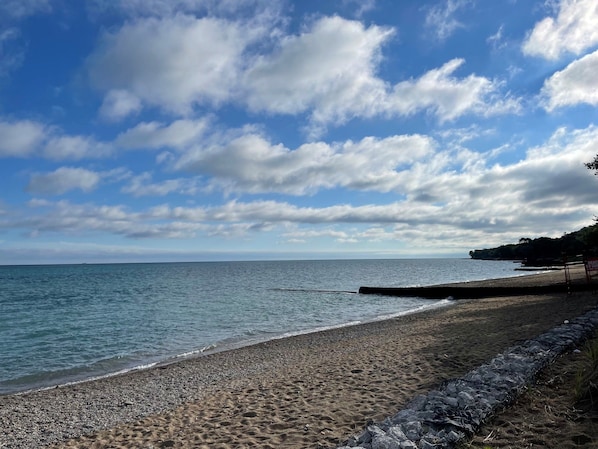 A beach with a rocky shoreline, a wooden jetty, and a sign indicating beach access.