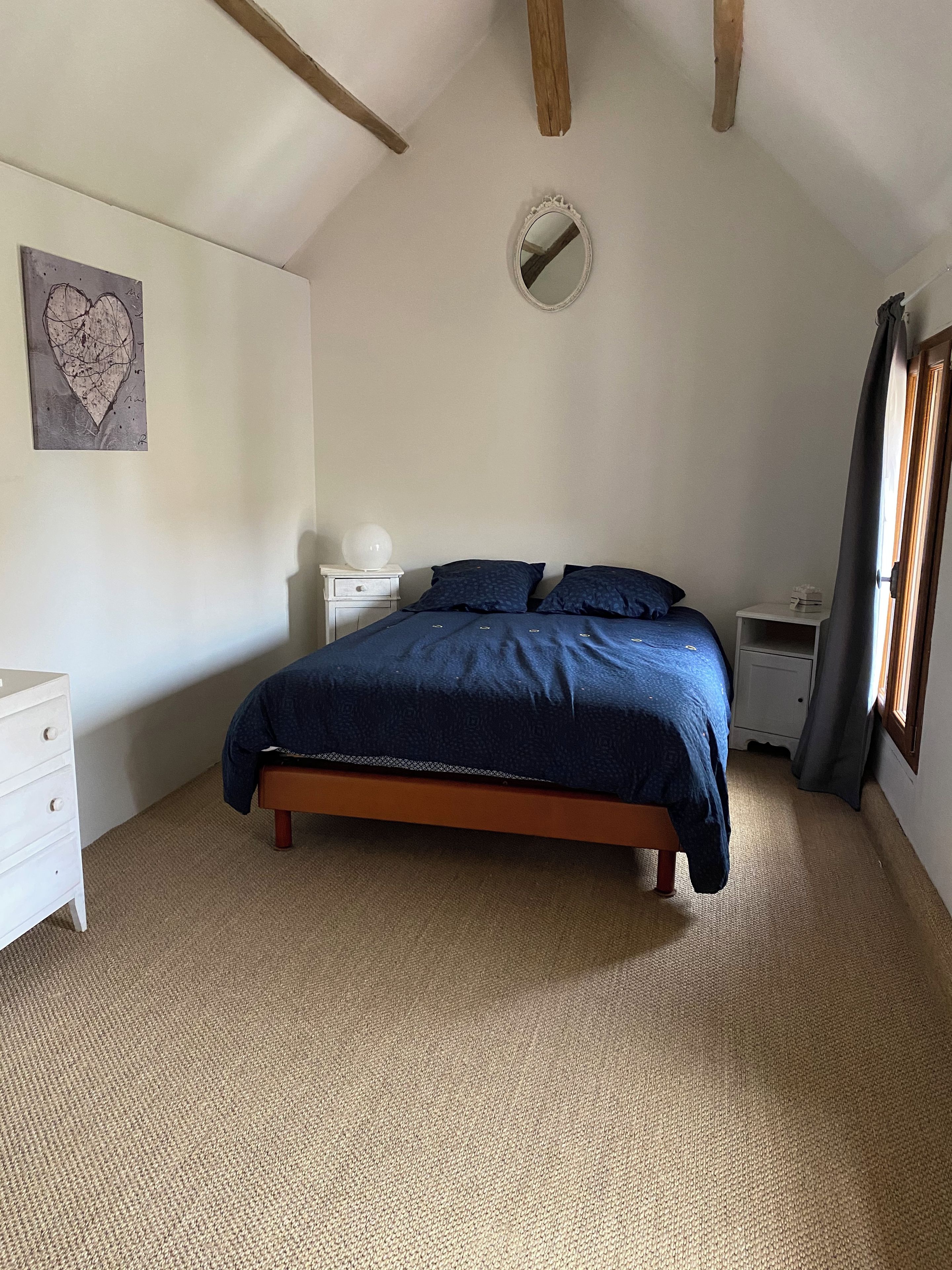 Un dormitorio con cama, mesitas de noche, un espejo en la pared y una obra de arte en la pared.