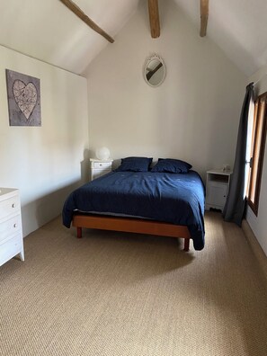 A bedroom with a bed, bedside tables, a nightstand, a wall-mounted mirror, and a piece of wall art.
