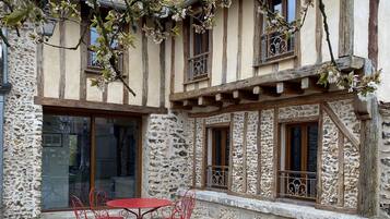 Un edificio de piedra tradicional con balcón, una mesa de madera con sillas y suelo de grava.