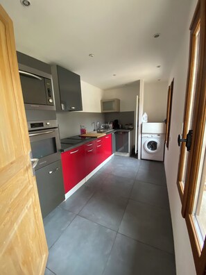 A modern kitchen with grey and red cabinetry, stainless steel appliances, and a built-in washing machine. - maison 4 couchages avec cour extérieur et parking (Bû)