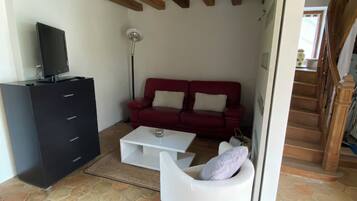 Una sala de estar con sofá rojo, sillón blanco, mueble multimedia negro y piso de baldosas.