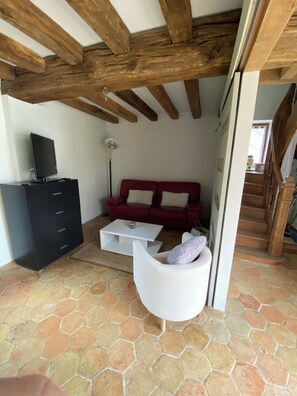 A living room with a red sofa, white armchair, black entertainment unit, and a tiled floor.