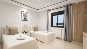 Une chambre d’hôtel avec deux lits, une fenêtre avec des rideaux, un radiateur et une armoire en bois.