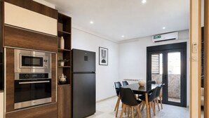 Une cuisine moderne dotée d’appareils électroménagers intégrés, un coin repas avec une table et des chaises, et une porte-fenêtre coulissante donnant sur un espace extérieur.